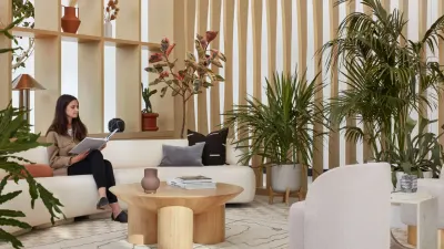 Sala de descanso con sofá blanco, mesa baja de madera, celosía de listones y muchas plantas; una mujer lee sentada.
