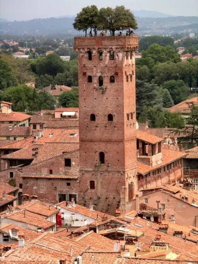 Torre Guinigi de Lucca: torre medieval de ladrillo coronada por árboles, con visitantes arriba y techos de tejas alrededor.