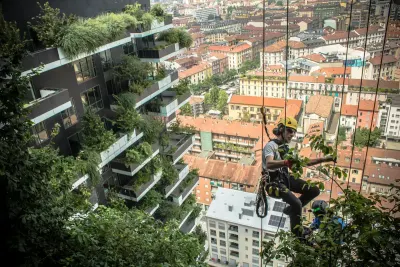 Un jardinero colgado de una cuerda poda las plantas del Bosco Verticale, con los techos de Milán de fondo