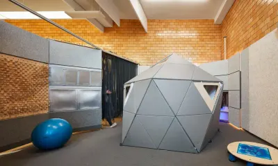 Sala sensorial con un domo geodésico de paneles de fieltro gris, pared táctil con relieves, pelota de ejercicio y una mesa con gel azul.
