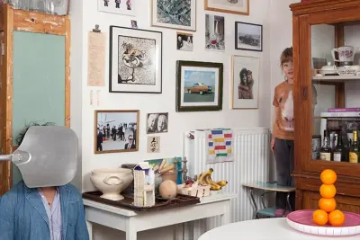 Rincón de una casa llena de vida: cuadros y fotos en la pared, una mesa con frutas y cuencos, un aparador antiguo y un chico que se asoma.