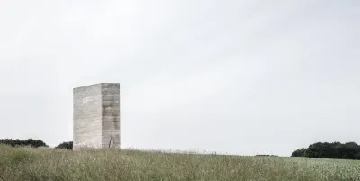 Capilla de Campo Bruder Klaus de Peter Zumthor: prisma de hormigón solitario en un campo de pastos altos bajo un cielo blanco.