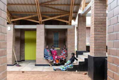 Cuatro mujeres sentadas en la galería de ladrillo de una de las casas, junto a una puerta verde, bajo el alero.