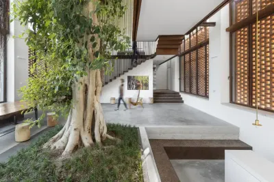 Interior de la Residencia Greenary: un gran ficus crece desde un cantero en el centro de la casa, junto a una escalera y muros de ladrillo calado.