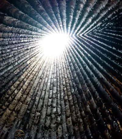 Interior de la capilla Bruder Klaus visto hacia arriba: paredes negras con la marca de los troncos que convergen en una abertura luminosa al cielo.