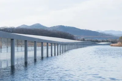 Zaishui Art Museum de Junya Ishigami: largo volumen delgado sobre pilares finos que se extiende sobre el agua, con cerros de fondo.