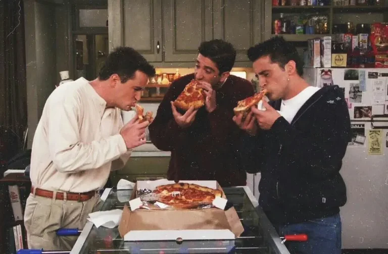 Escena de Friends: Joey, Chandler y Ross comiendo pizza de pie.